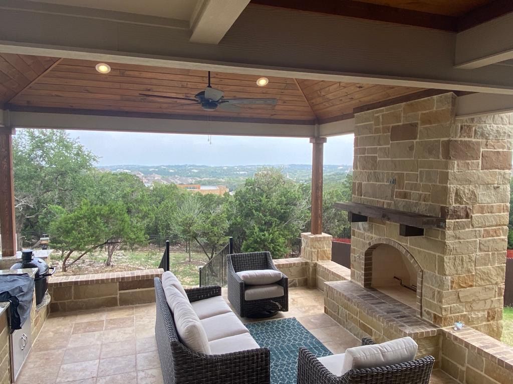 A patio with a fireplace , couch , chairs and a ceiling fan built by Fine Patio Design San Antonio TX