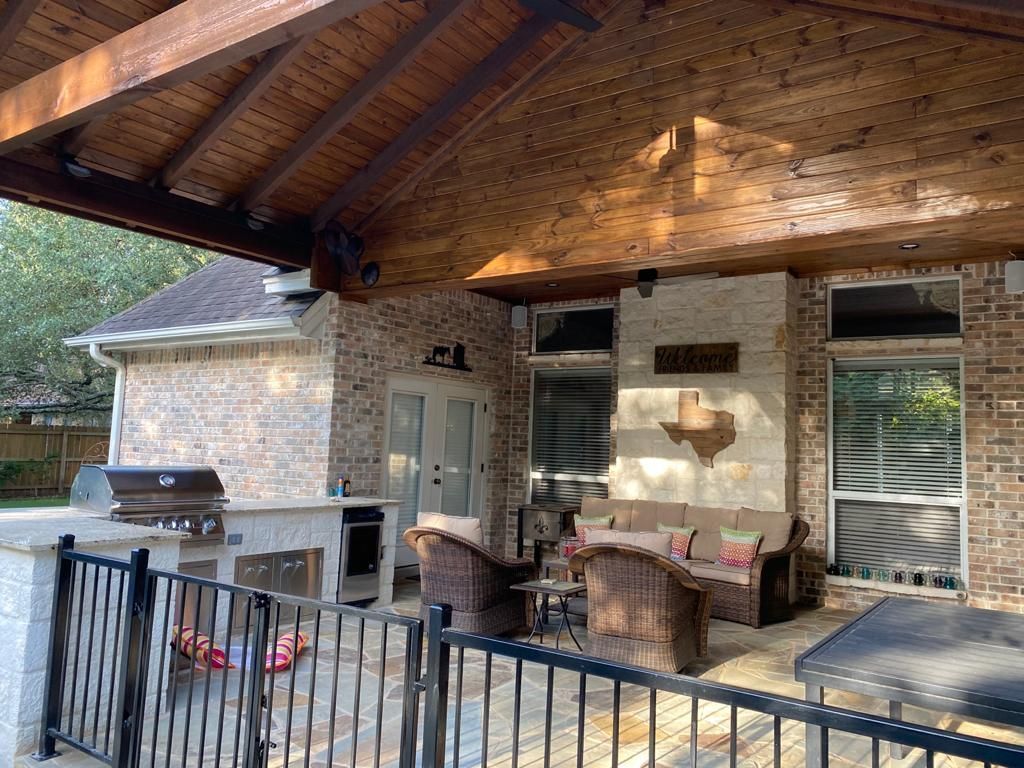A patio with a couch and chairs under a wooden roof built by Fine Patio Design San Antonio TX