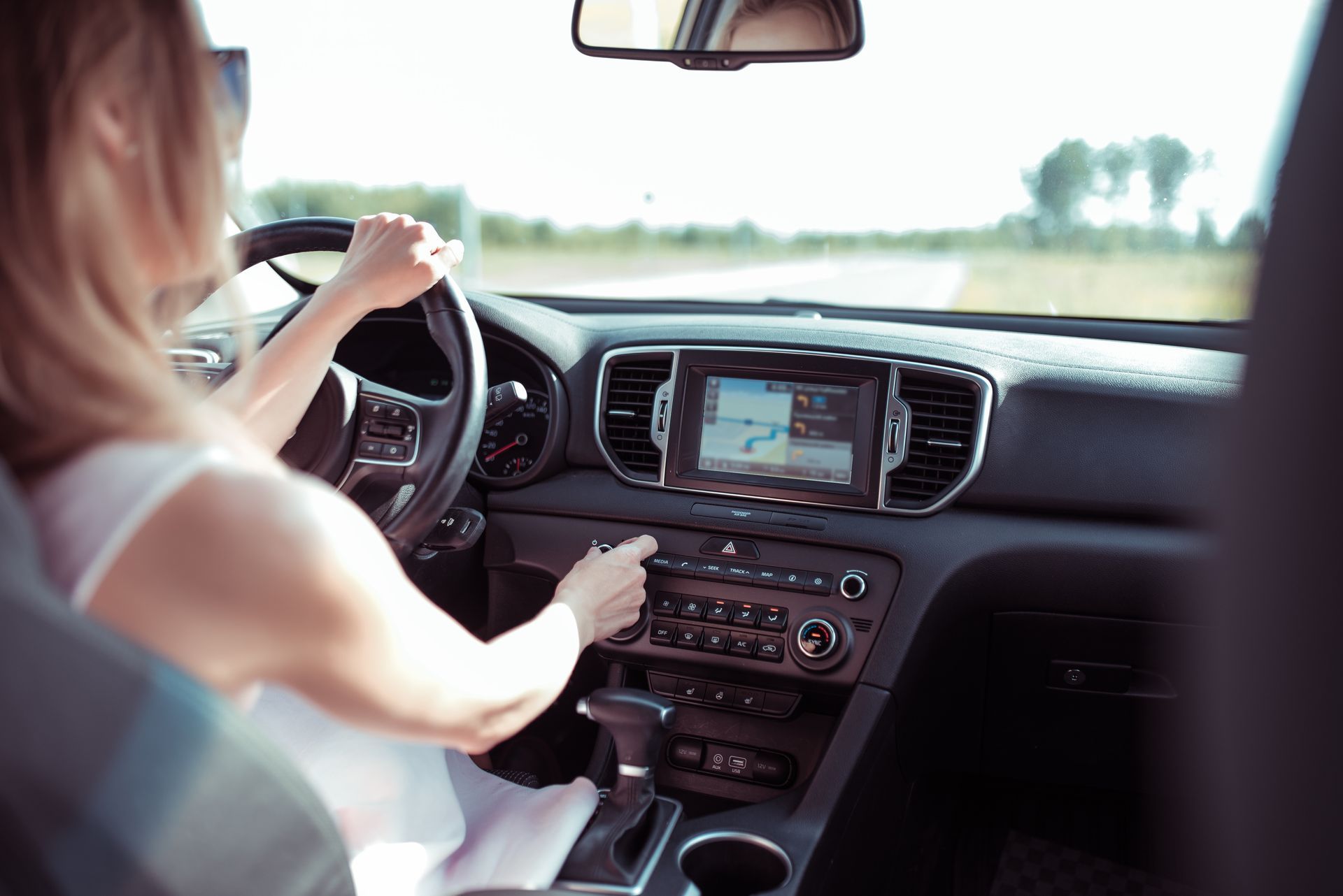 A woman is driving a car and adjusting the Air conditioning