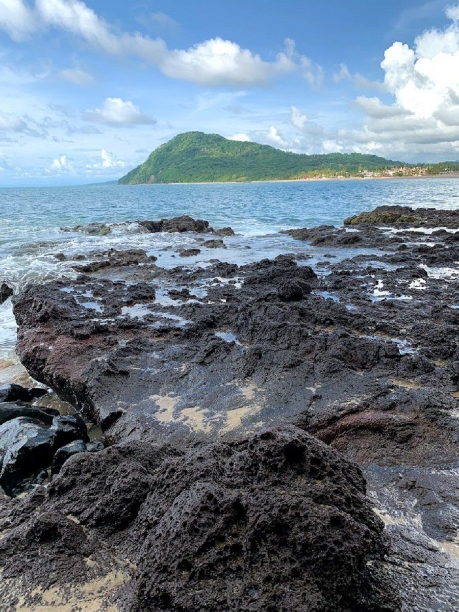 A rocky beach with a mountain in the background and a large body of water.
