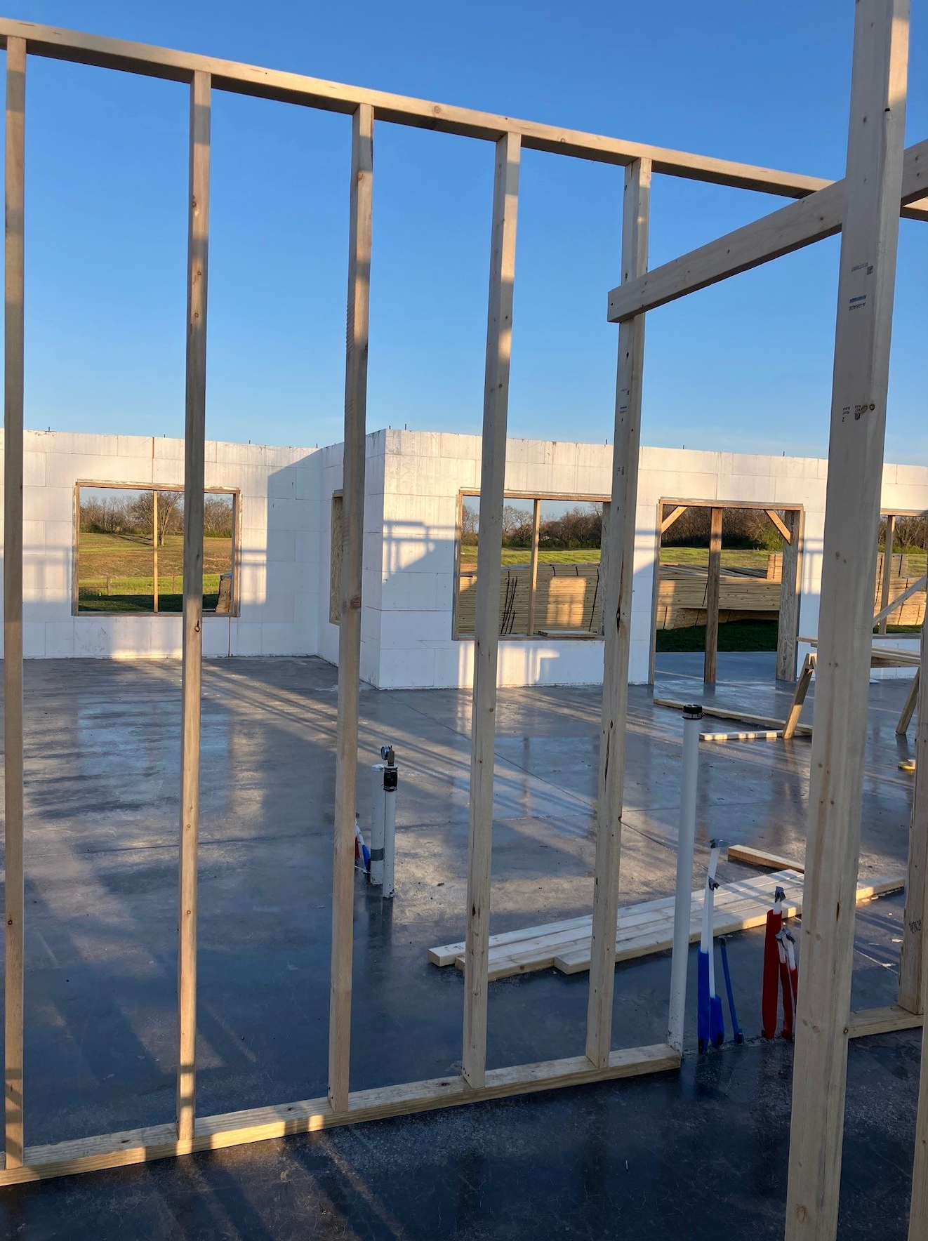 Partially built rooftop with white framing, a concrete floor, and a city view under a blue sky