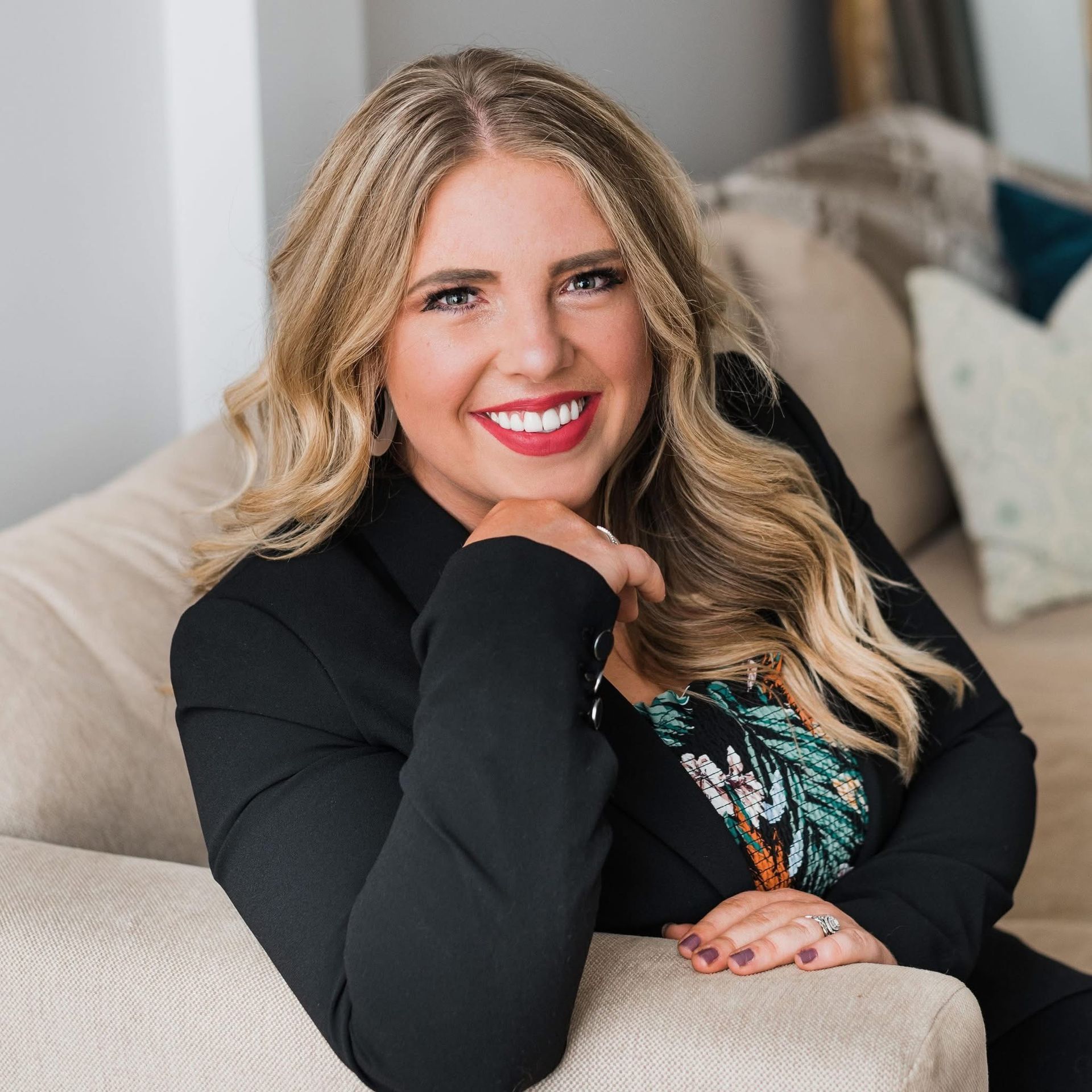 Smiling woman in a black blazer leaning on a sofa in a bright living room