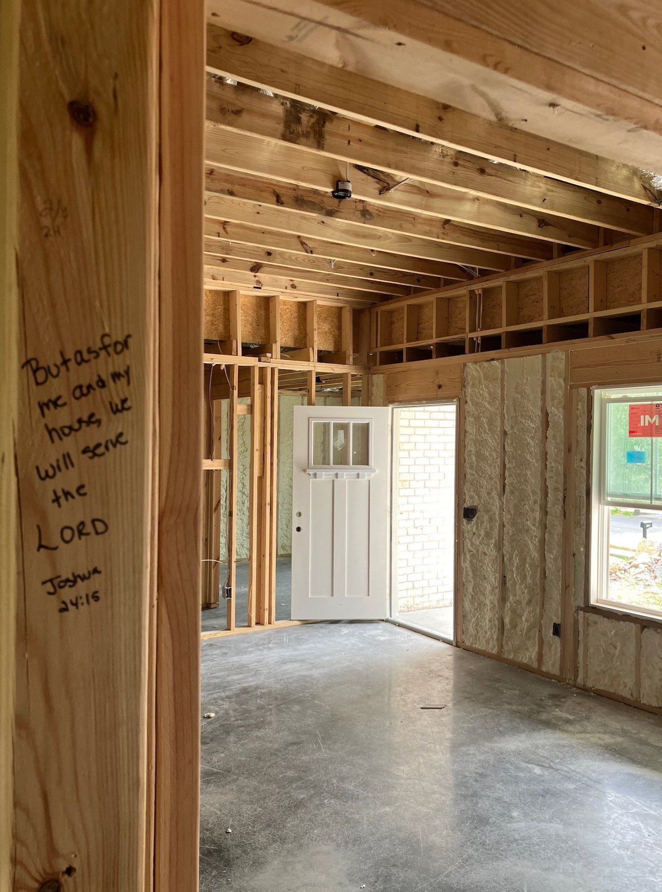 Unfinished room with exposed wood framing, a white door, concrete floor, and window light
