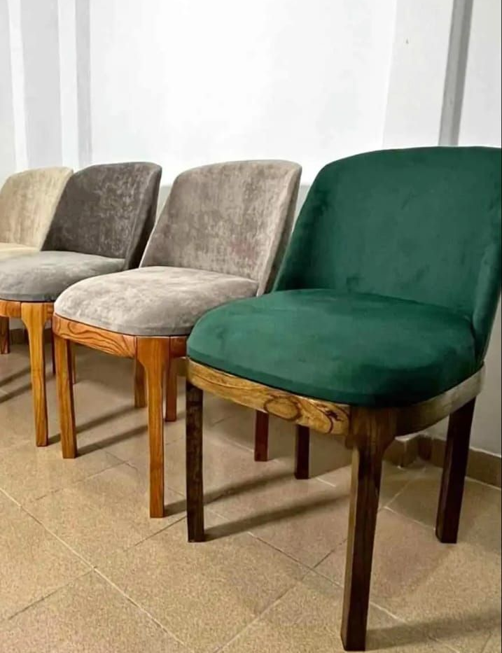 Tres sillas de comedor tapizadas con patas de madera alineadas sobre un suelo de baldosas, una silla verde oscuro delante.