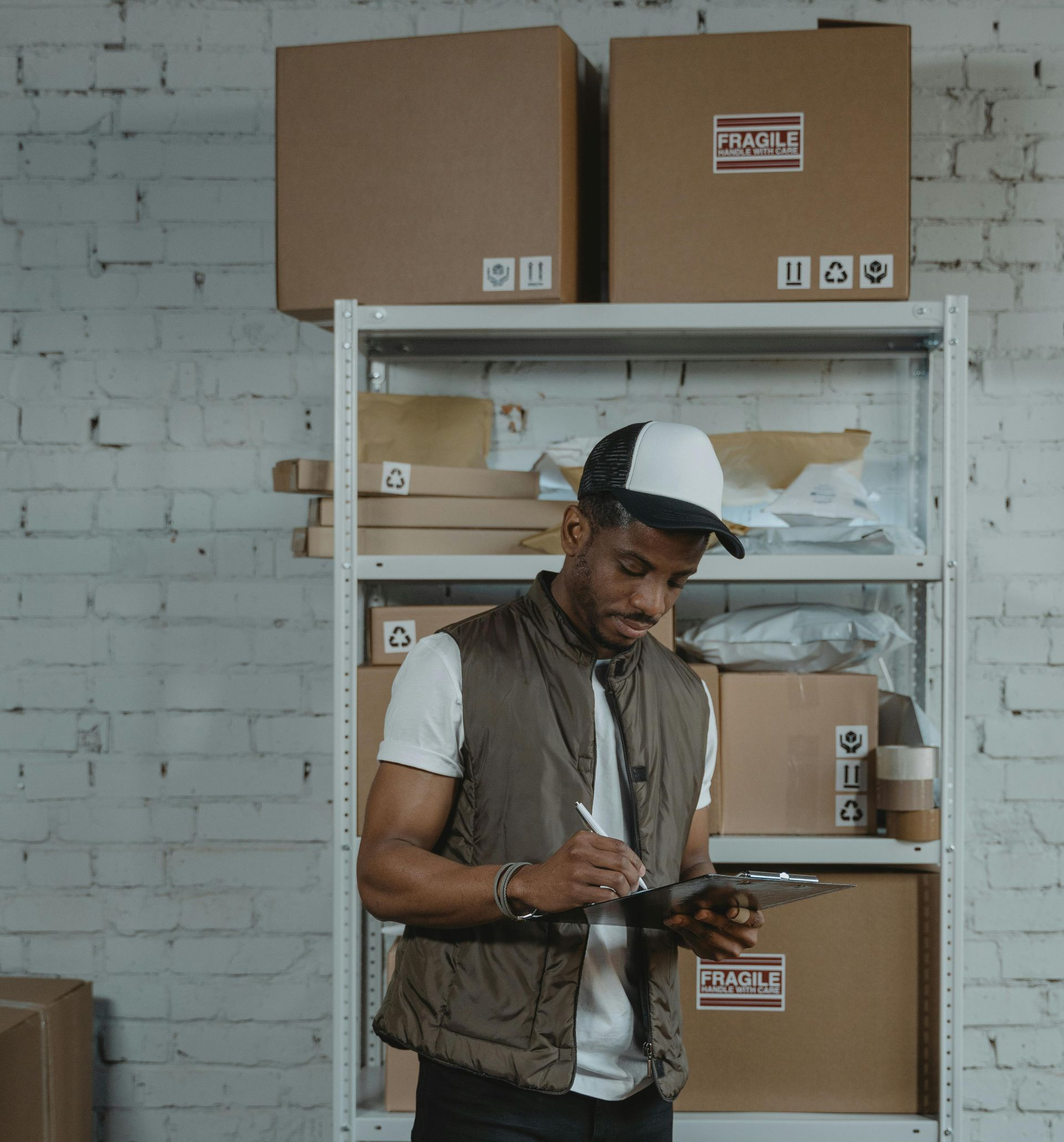 Man writing on a clipboard in a small storage room with shelves and cardboard boxes