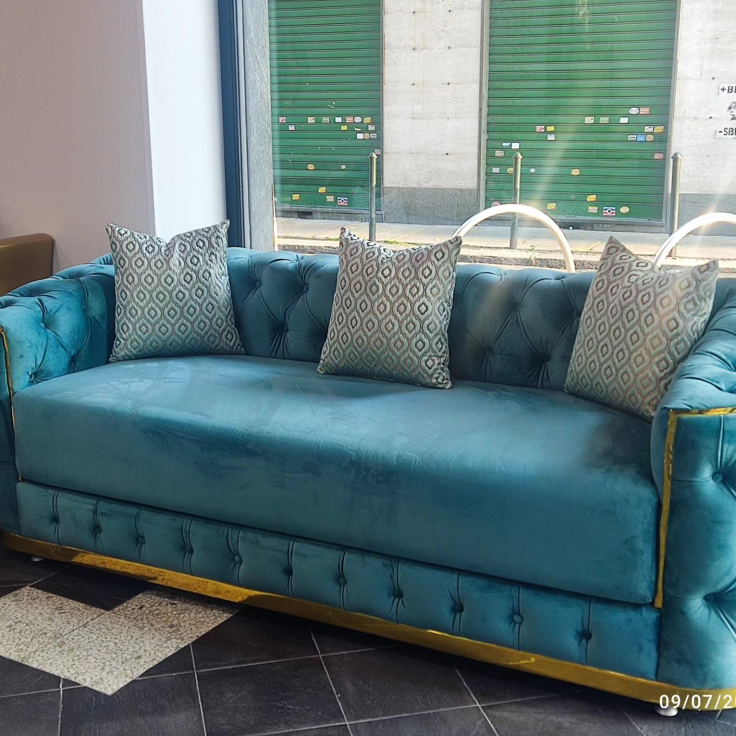 Un divano blu con dei cuscini è appoggiato davanti a una finestra.