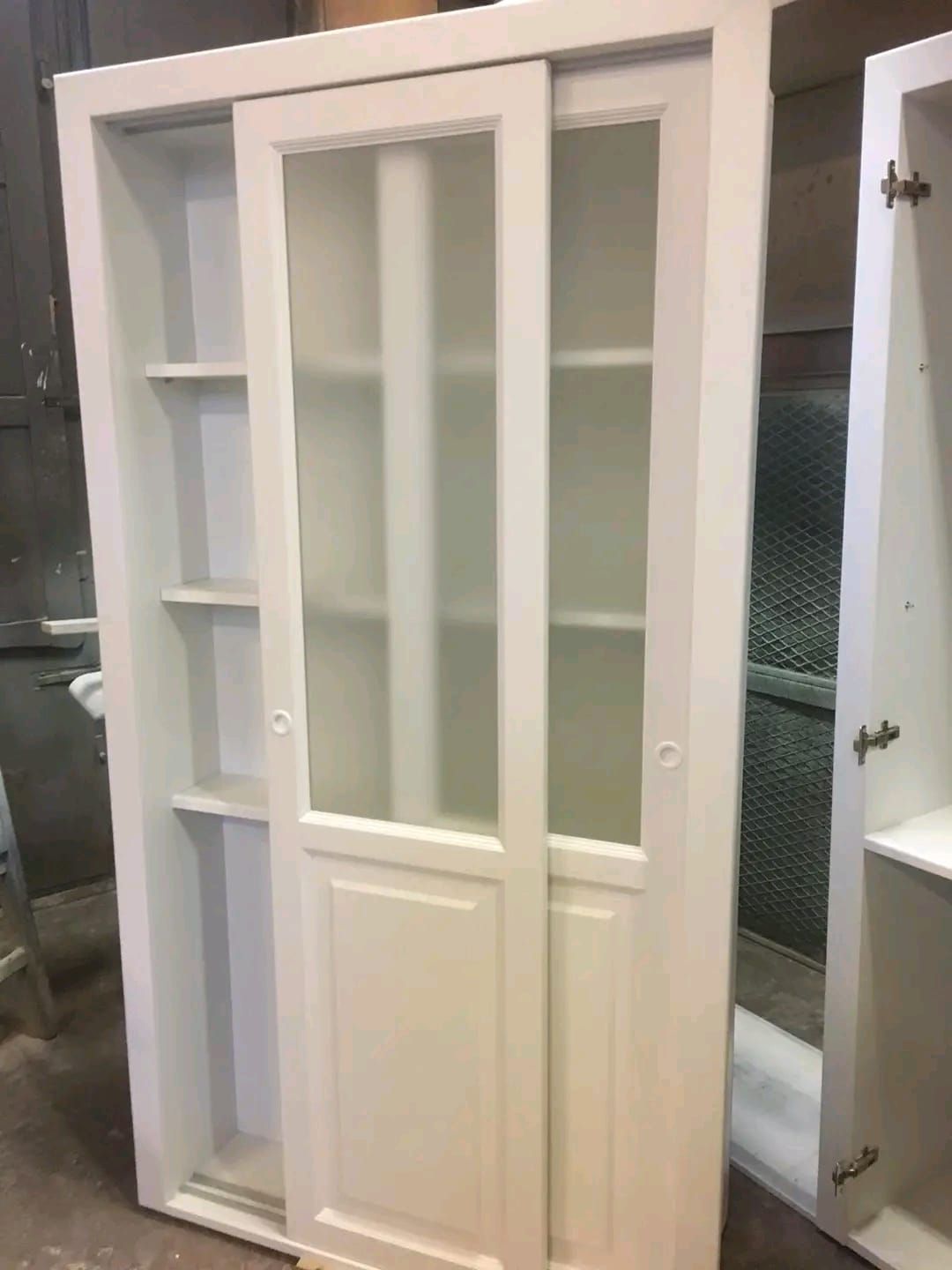 Un mobile bianco con ante scorrevoli in vetro e ripiani.