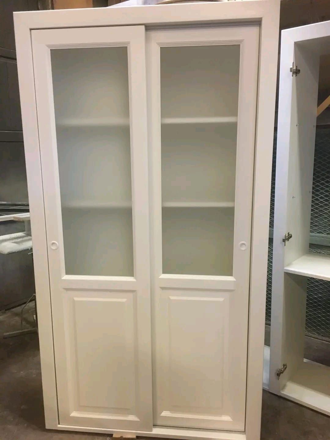 Un mobile bianco con ante scorrevoli in vetro e ripiani.