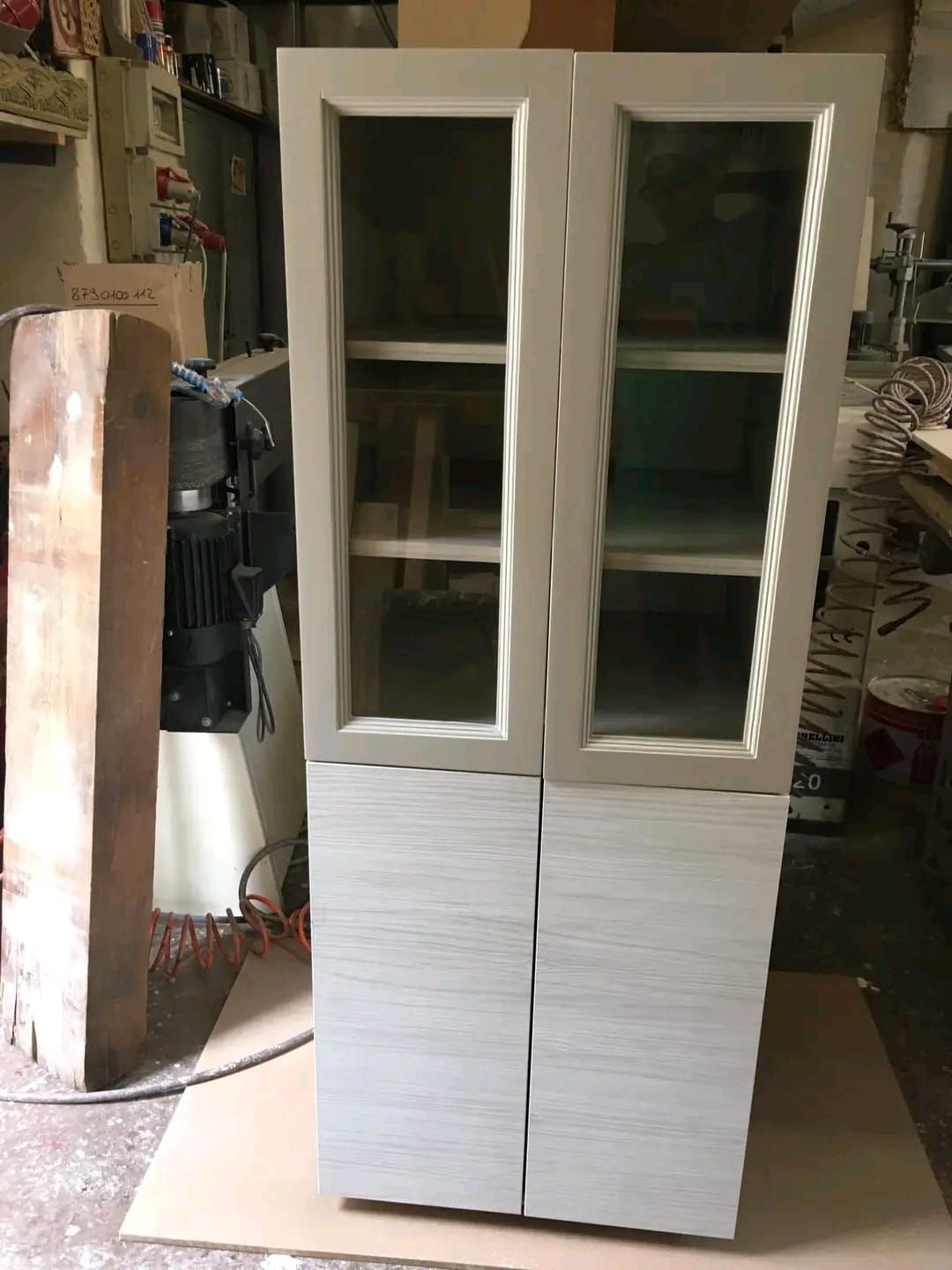 Un mobile bianco con ante in vetro è appoggiato su un tavolo in una stanza.