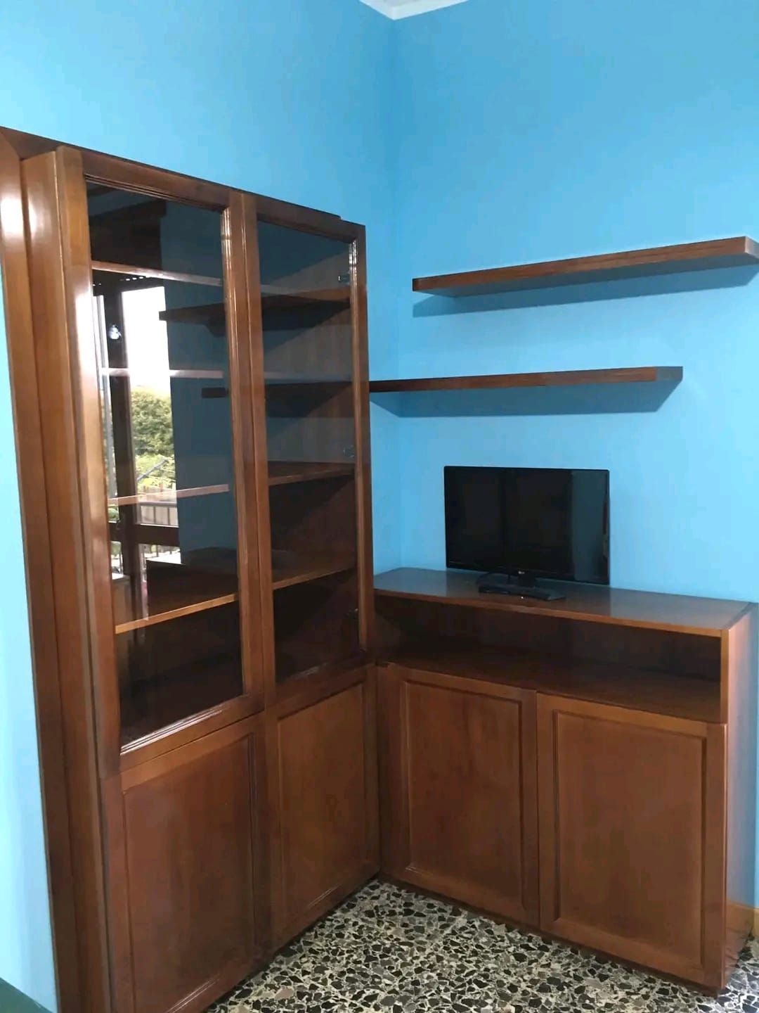 Un angolo di una stanza con scaffali e una tv