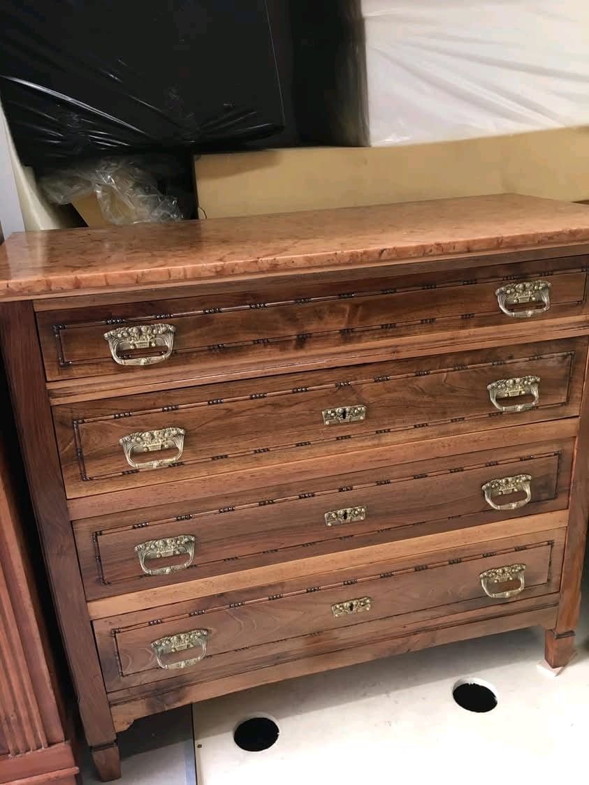 Una cassettiera in legno con quattro cassetti è appoggiata su un pavimento bianco.