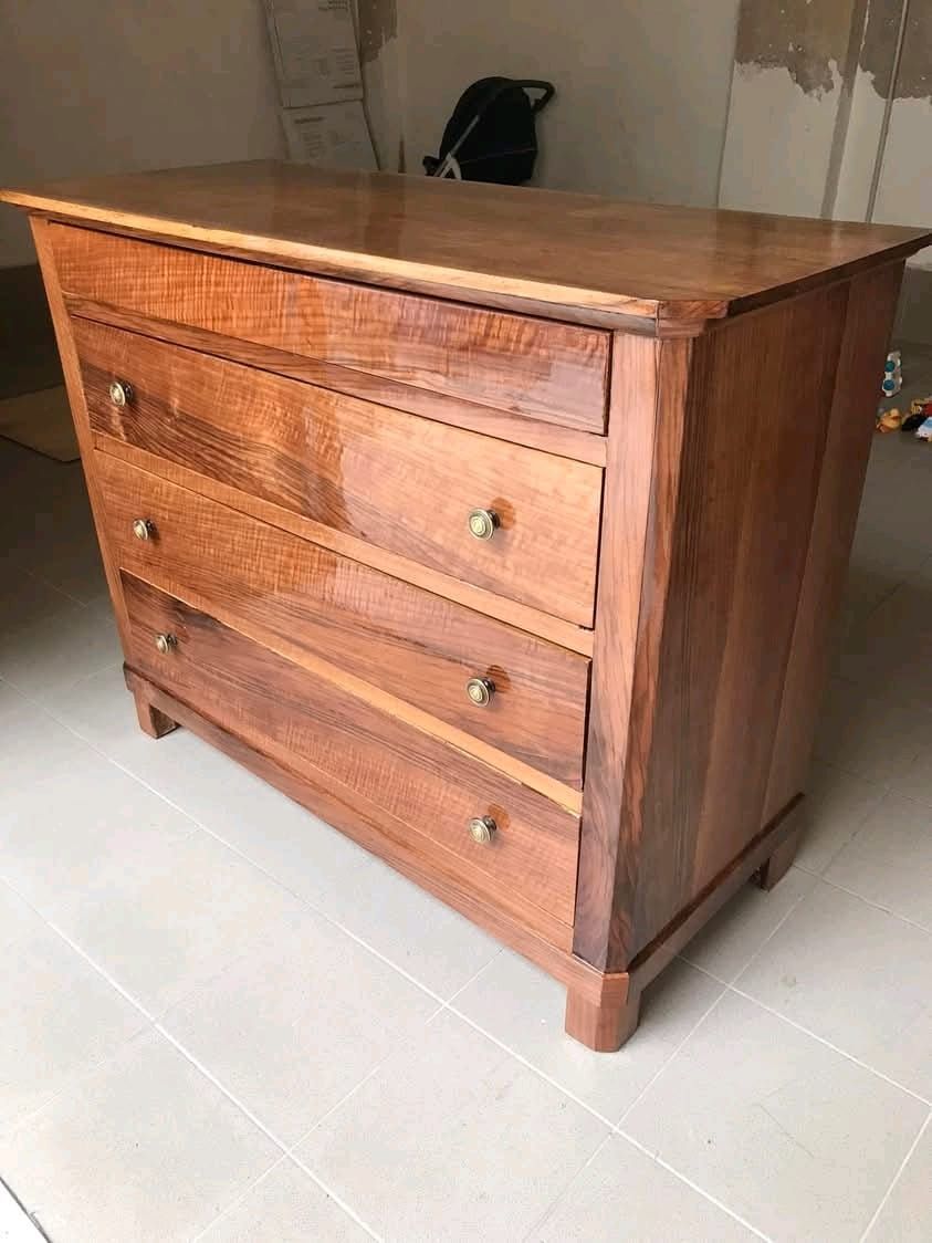 In una stanza c'è una cassettiera di legno con quattro cassetti appoggiata sul pavimento piastrellato.