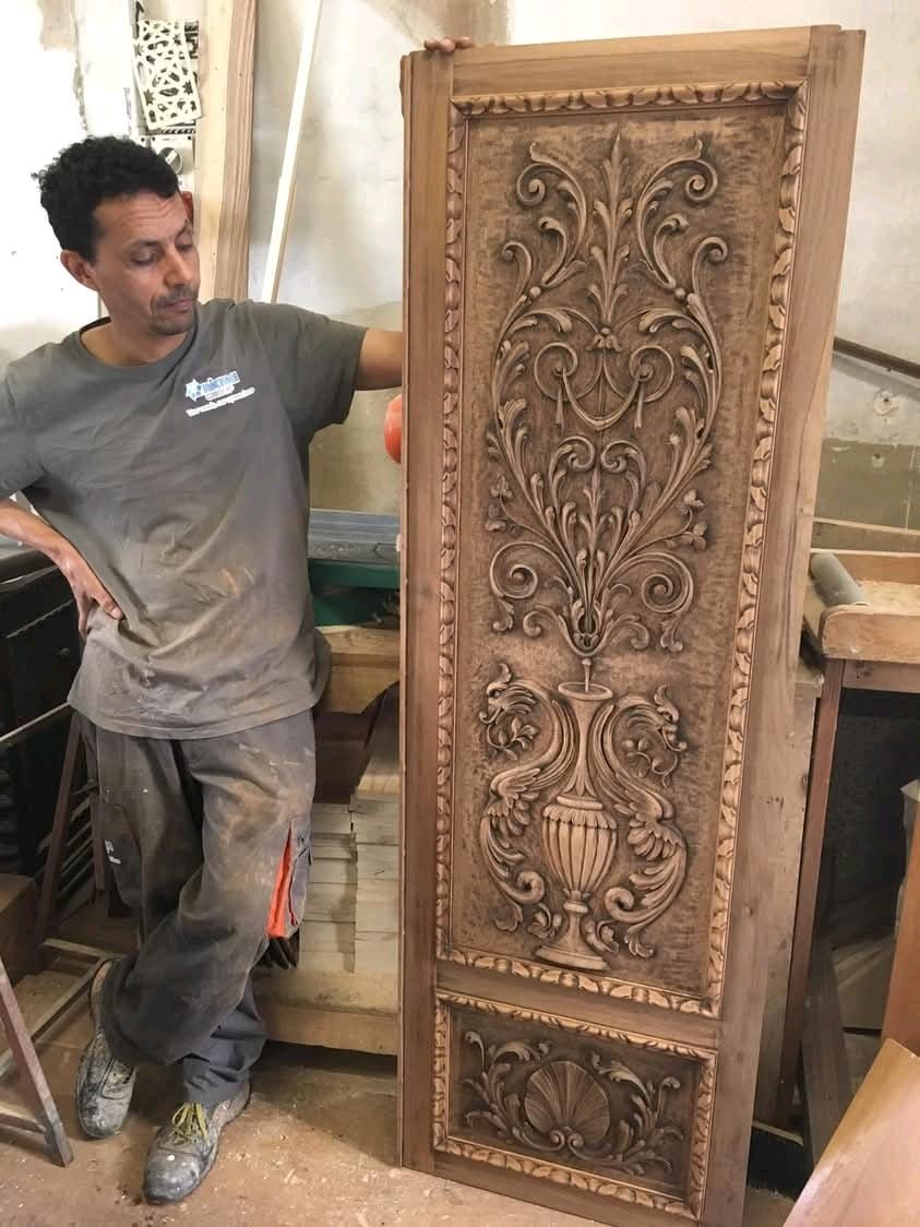 Un uomo è in piedi accanto a una porta di legno intagliata.