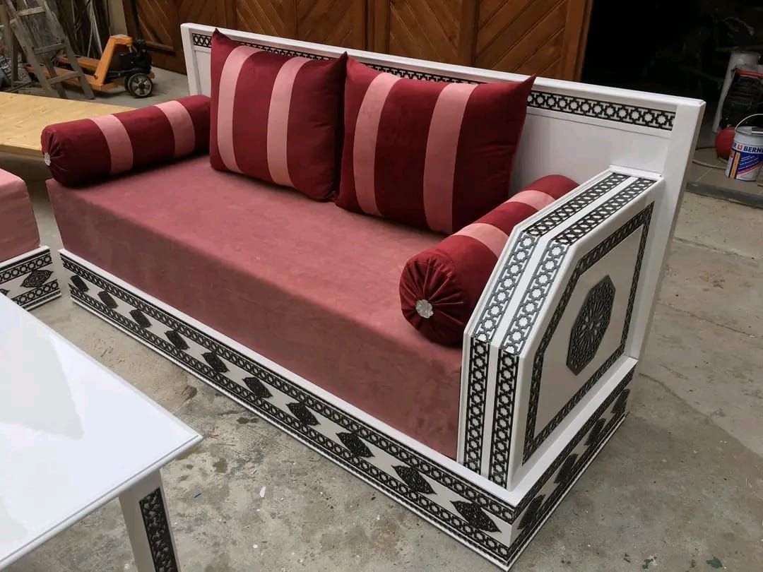 Un divano rosa con cuscini rossi e bianchi è appoggiato accanto a un tavolo bianco.