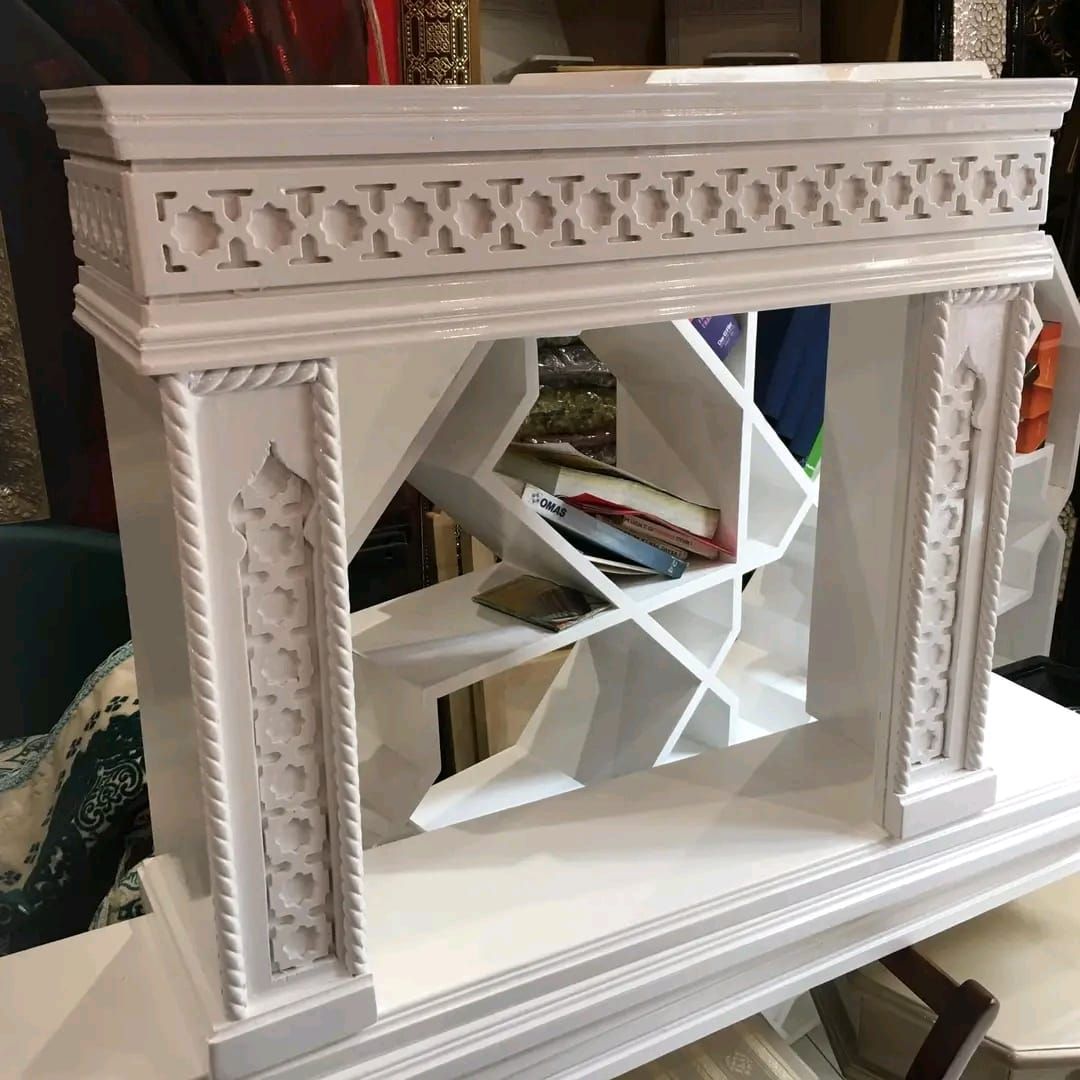 Una mensola per camino bianca è appoggiata su un tavolo accanto a una libreria.