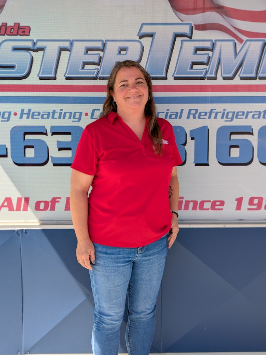 Woman in a red polo and jeans standing in front of a business sign.
