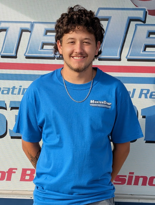 Smiling person in a blue T-shirt standing in front of a branded backdrop.