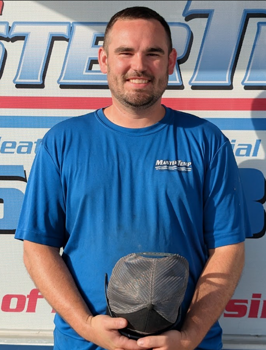 Smiling person in a blue shirt holding a black cap in front of a branded wall
