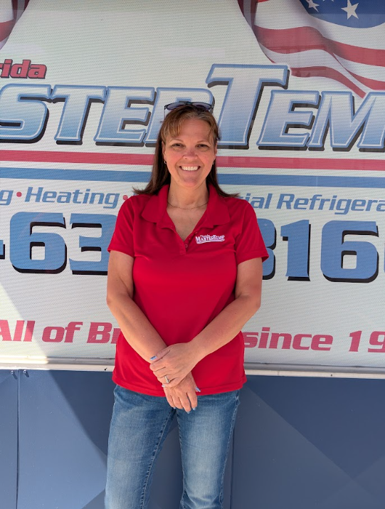 Woman in a red polo shirt stands smiling in front of a company banner.