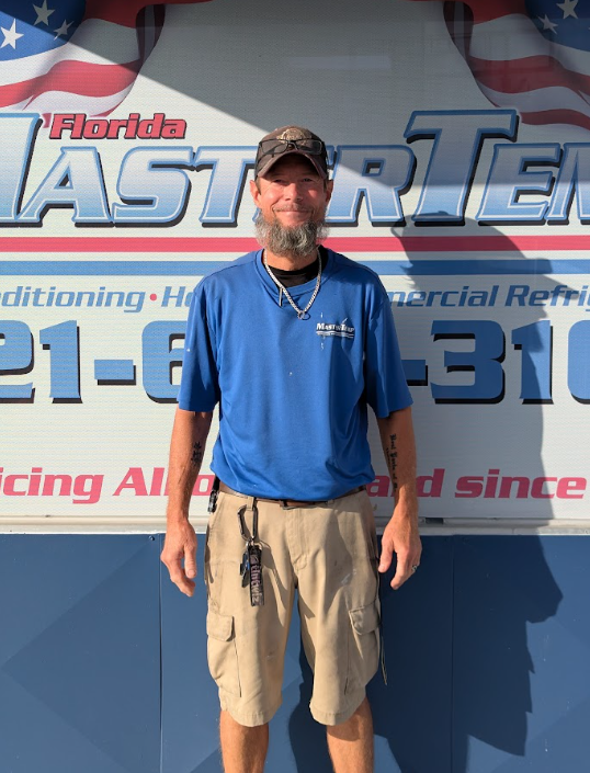 Man in blue polo and tan shorts standing before a Florida HVAC company banner