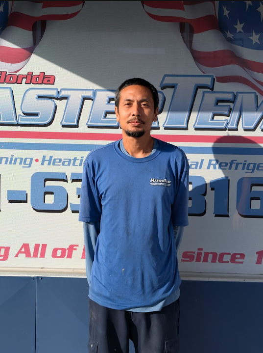 Man standing in front of a Master Temp HVAC service sign, wearing a blue shirt and cap.