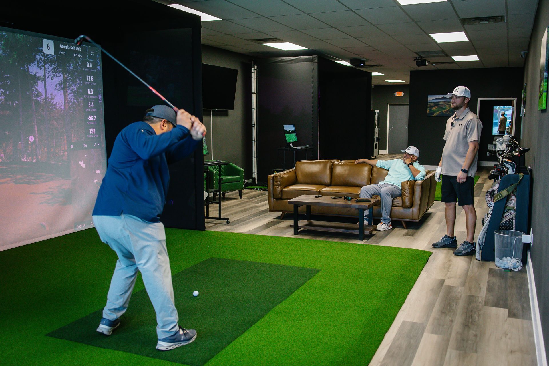 A man is swinging a golf club in a golf simulator.