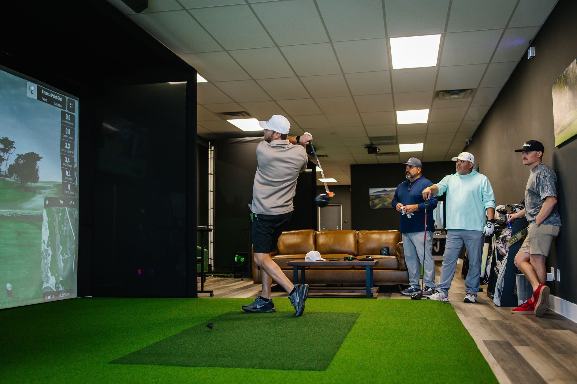 A group of men are playing golf in a simulator.