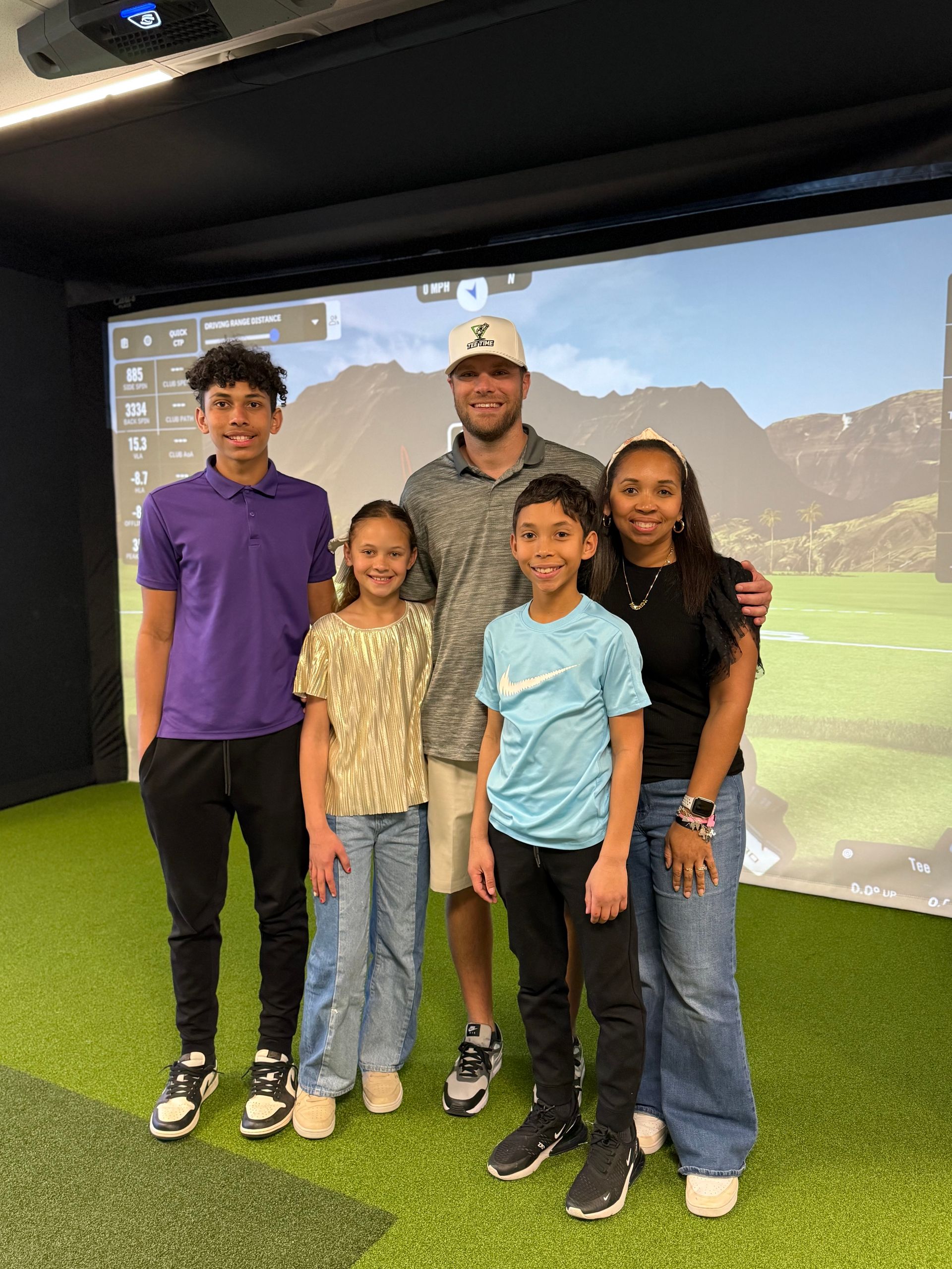 A man and three children are posing for a picture in a golf simulator.