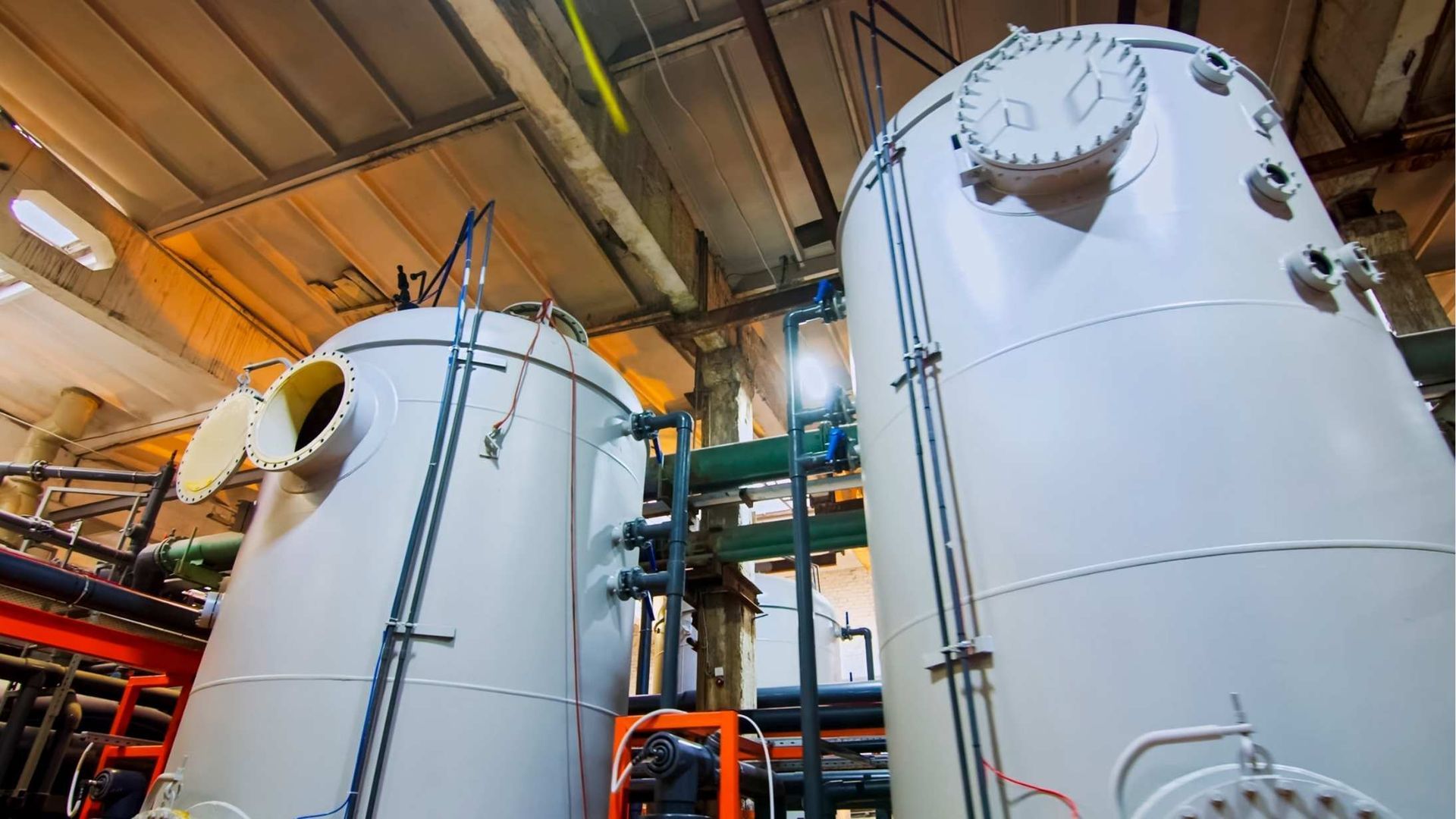 Two large white tanks are sitting next to each other in a factory.