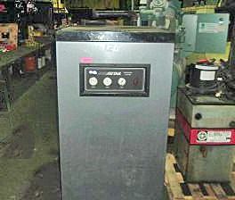 A large gray machine is sitting on top of a wooden pallet in a factory.