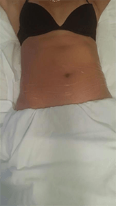 A woman in a black bra is laying on a bed with her arms outstretched.