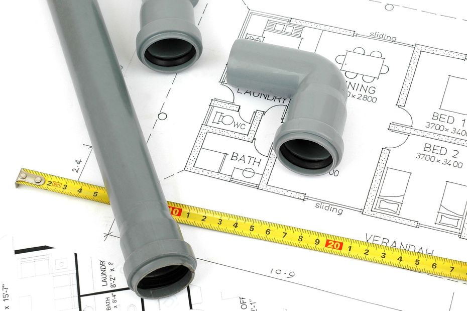 Tubi in PVC grigi e un metro a nastro giallo su planimetrie idrauliche.