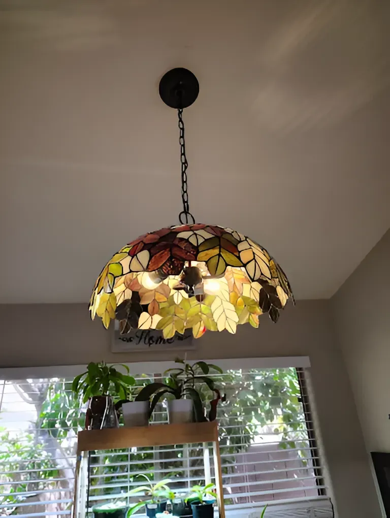 Tiffany-style pendant lamp with stained glass leaves.  Hangs over a plant stand near a window.