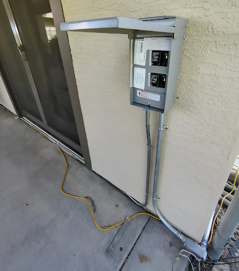 Gray electrical box mounted on a beige exterior wall, with conduit and power cables.