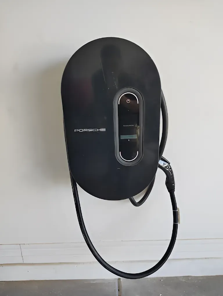 Black Porsche EV charger mounted on a white wall with the charging cable hanging down.