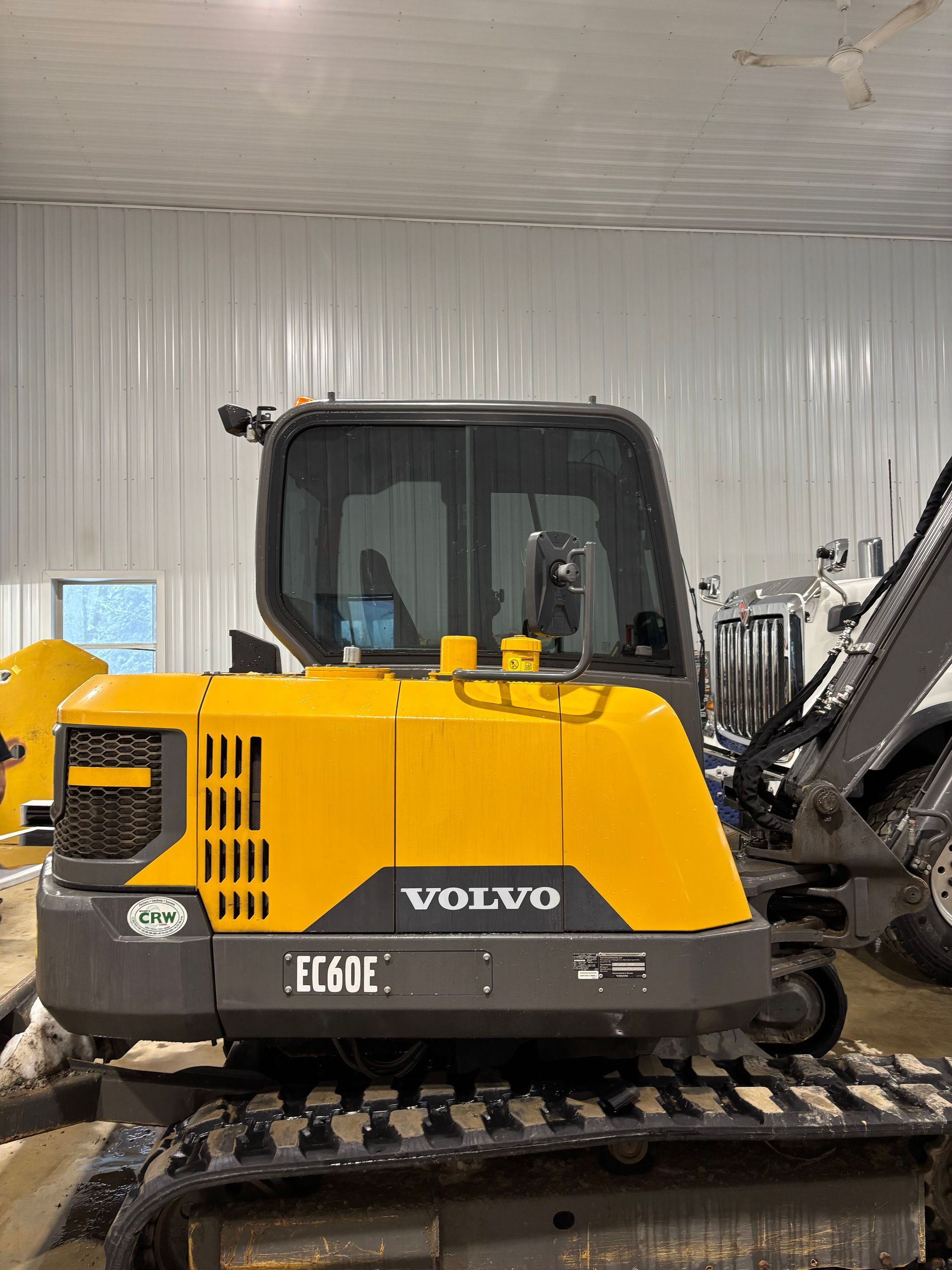 Yellow Volvo EC60E excavator in a building, with black tracks and a clear glass cabin.