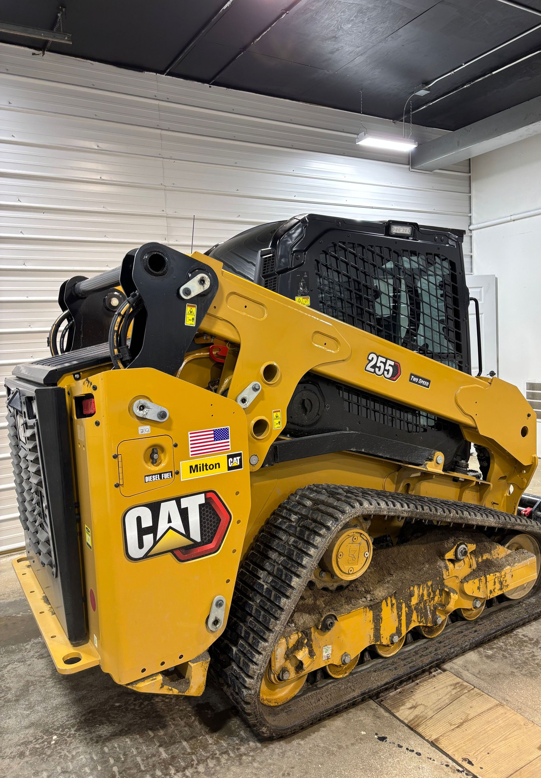 Yellow Caterpillar compact track loader inside a building, track treads and bucket arm details.