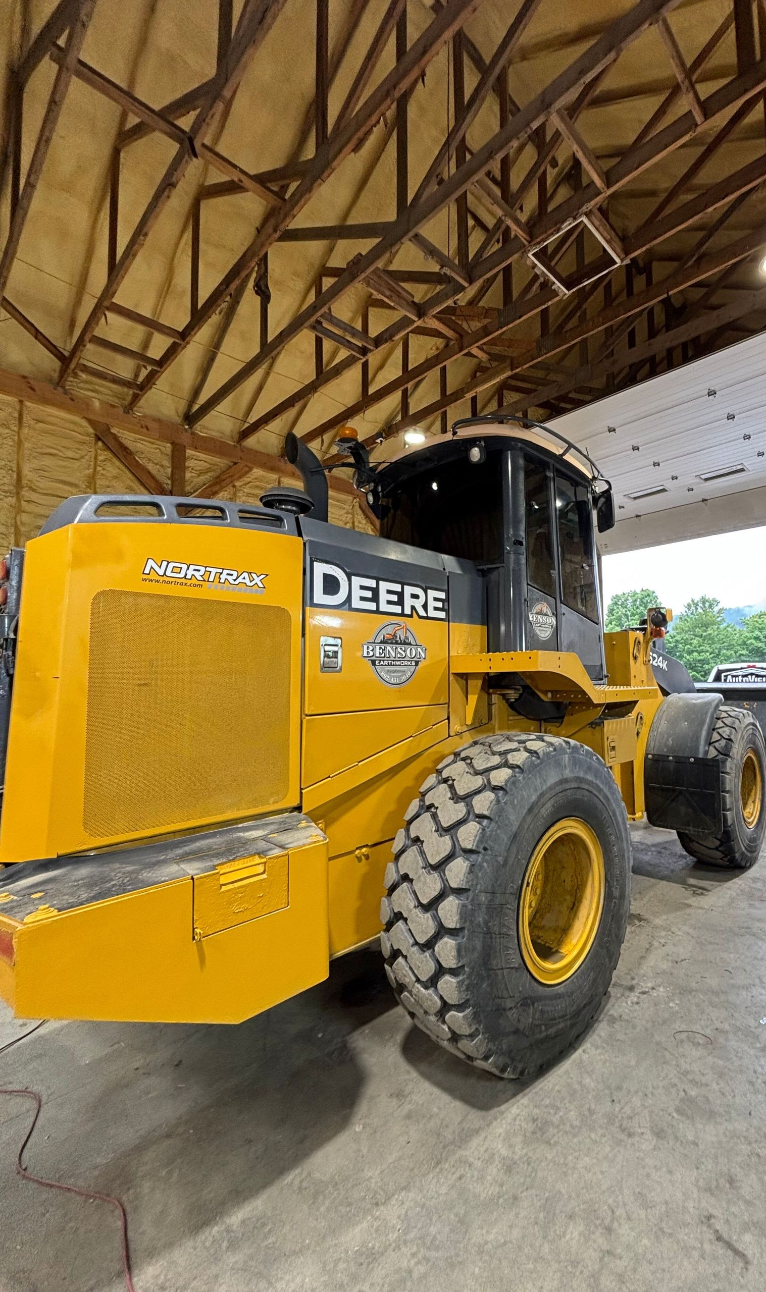 Yellow John Deere wheel loader exiting a barn. The open door reveals a parked truck outside.