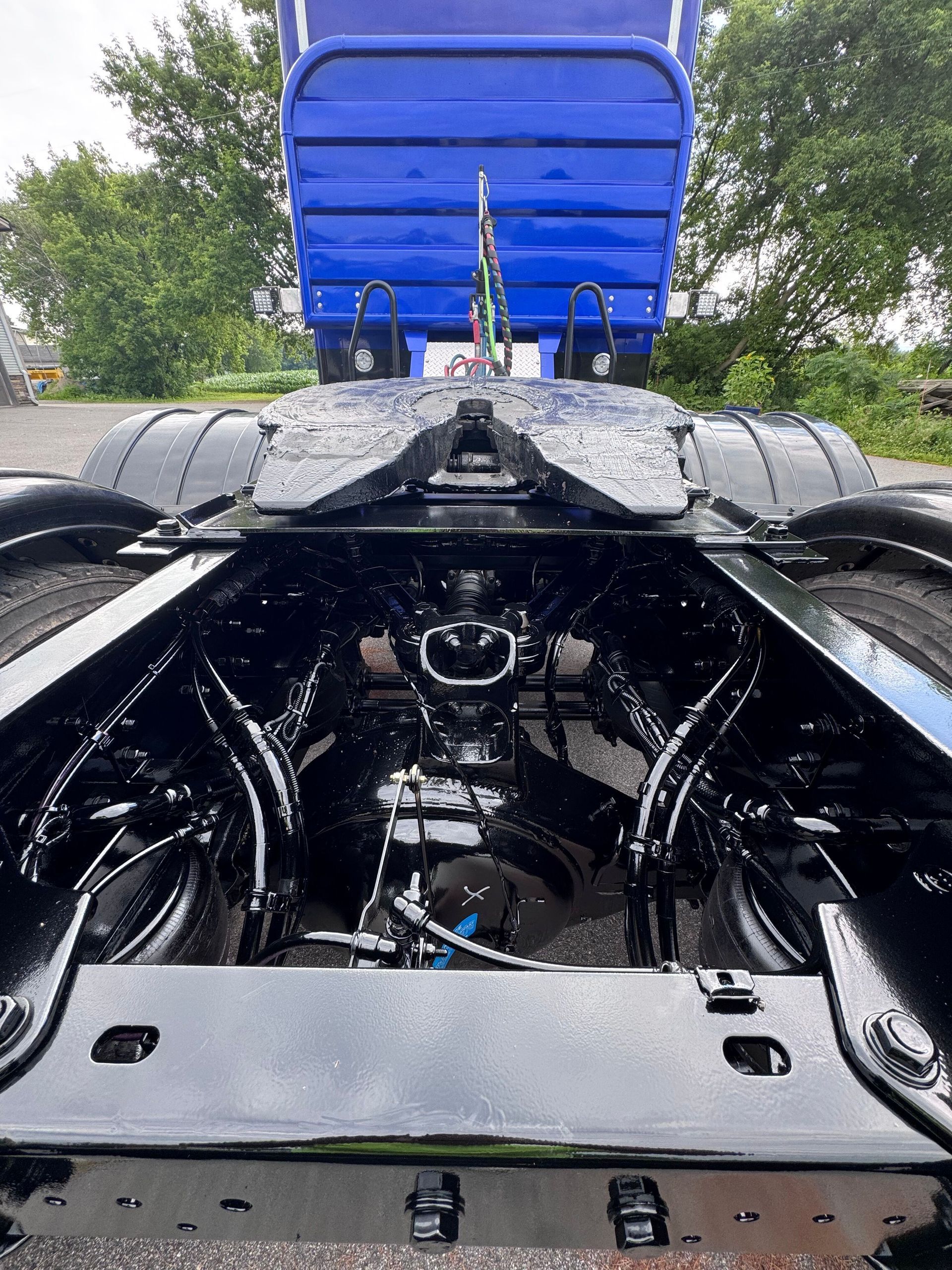 Black truck chassis with a blue trailer, viewed from underneath. Shows the fifth wheel coupling and other mechanical components.