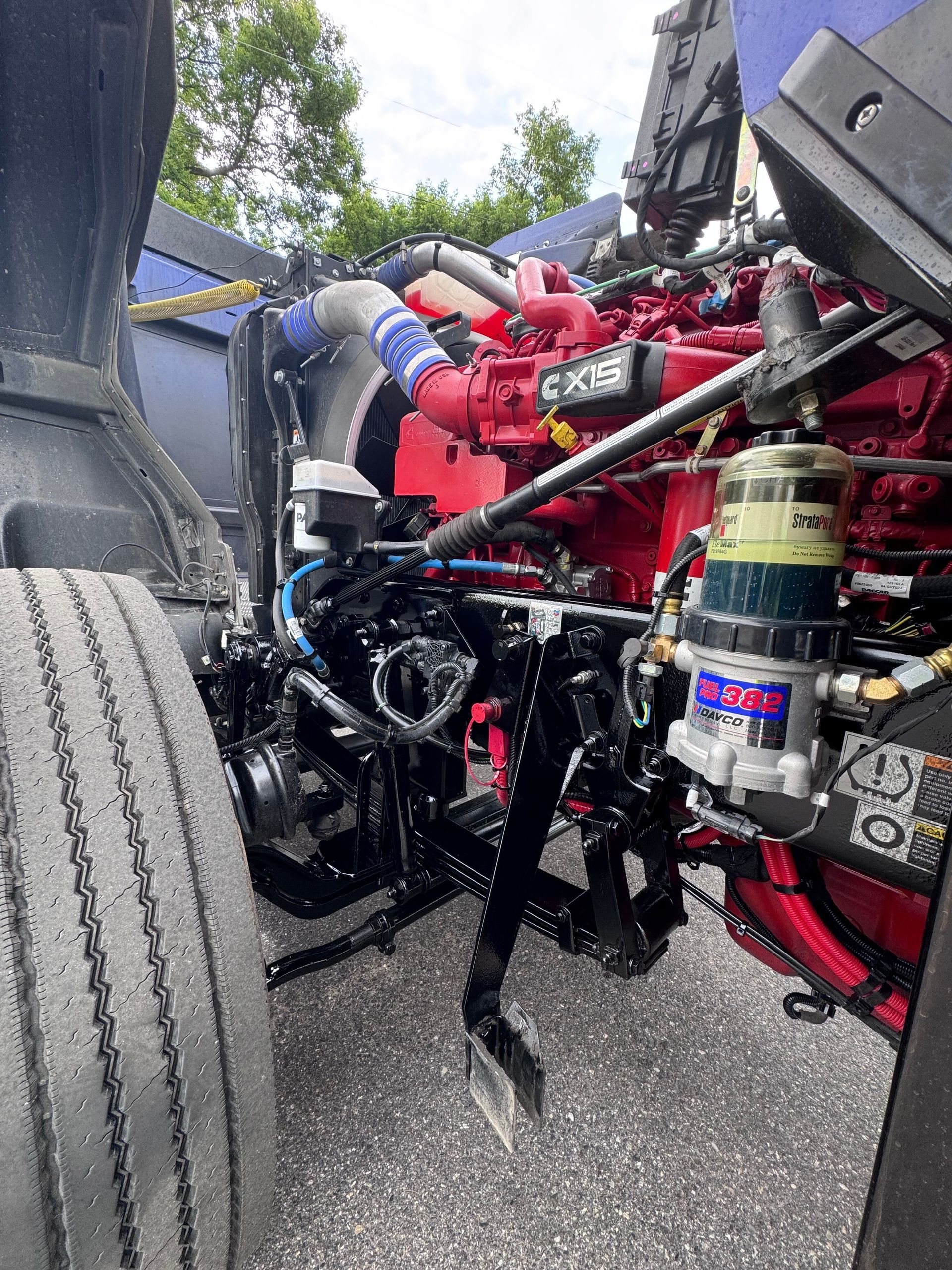 A truck engine compartment, with the hood open. The red engine has black and blue components.