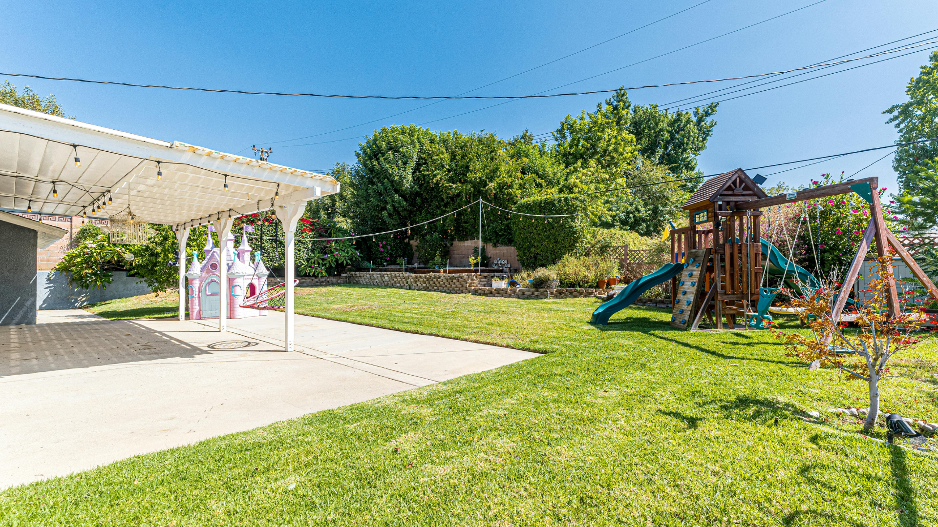 Sunny backyard playground with slide and swing set beside a covered patio and green lawn