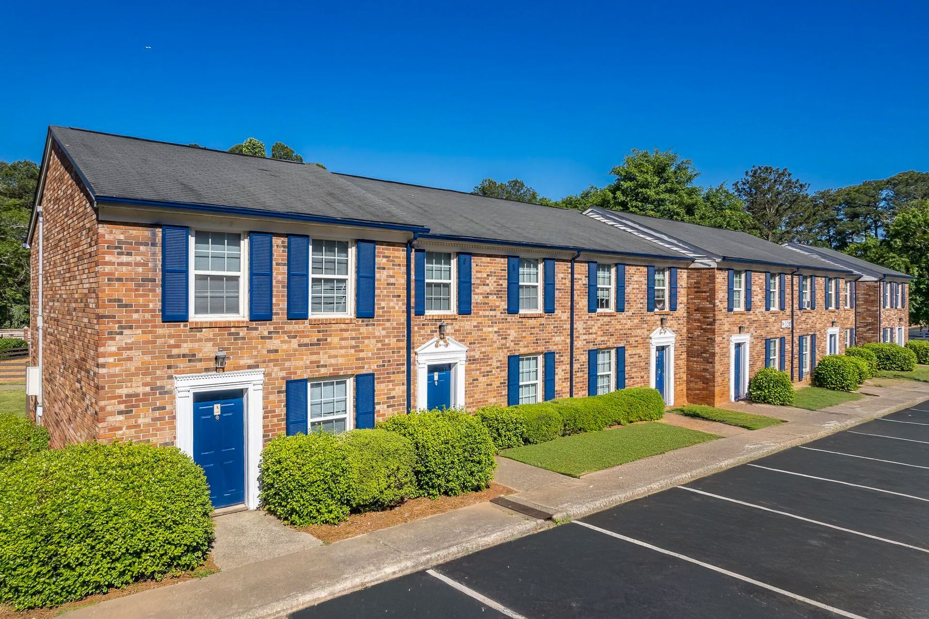 Ranch-style house with brick and gray exterior, pillars, surrounded by greenery and lawn.