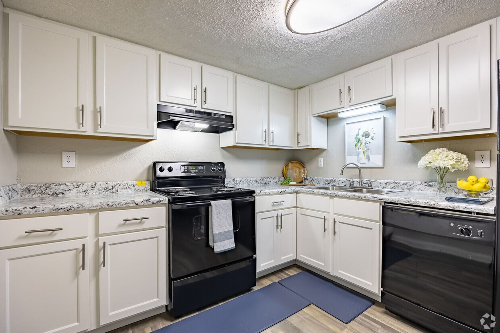 White kitchen with stainless steel appliances, cabinets, and light gray countertops.