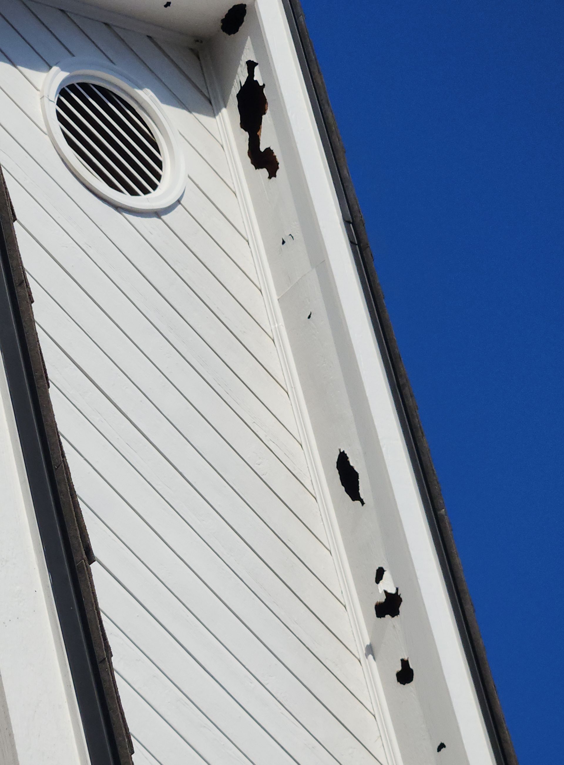 White house siding with round vent and black decorative brackets against a blue sky