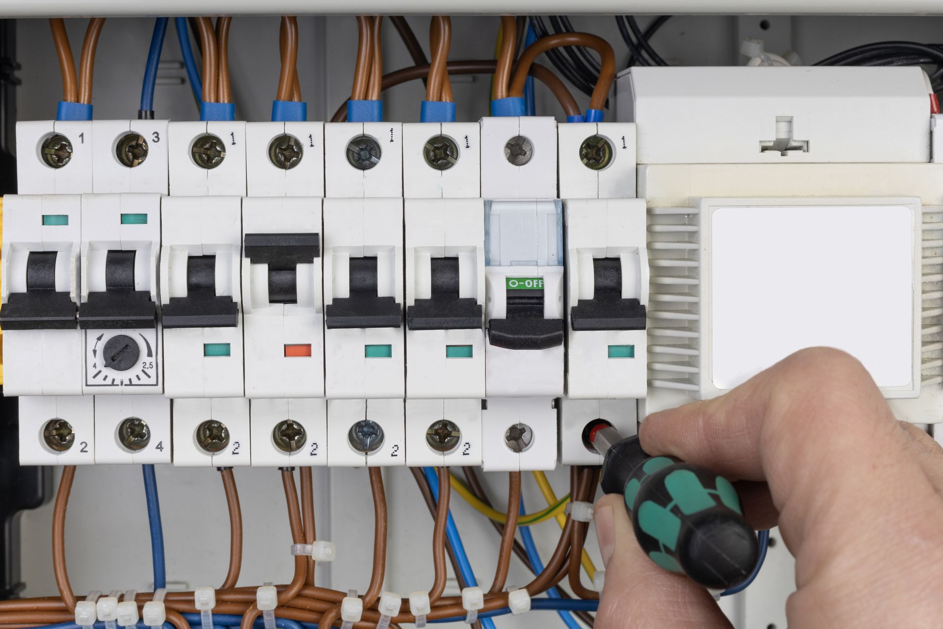 Hand tightening a screw on an electrical breaker panel with wires visible