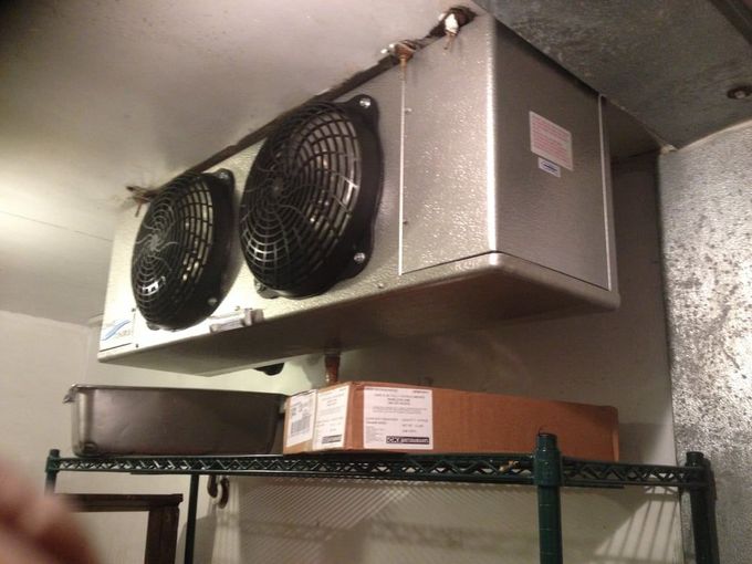 A refrigerator with two fans hanging from the ceiling