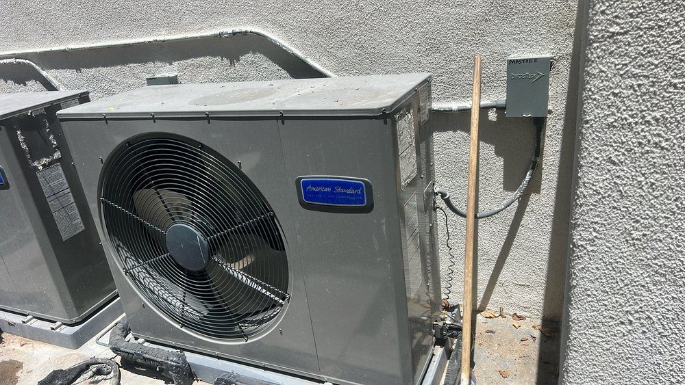 Two air conditioners are sitting next to each other on the side of a building.