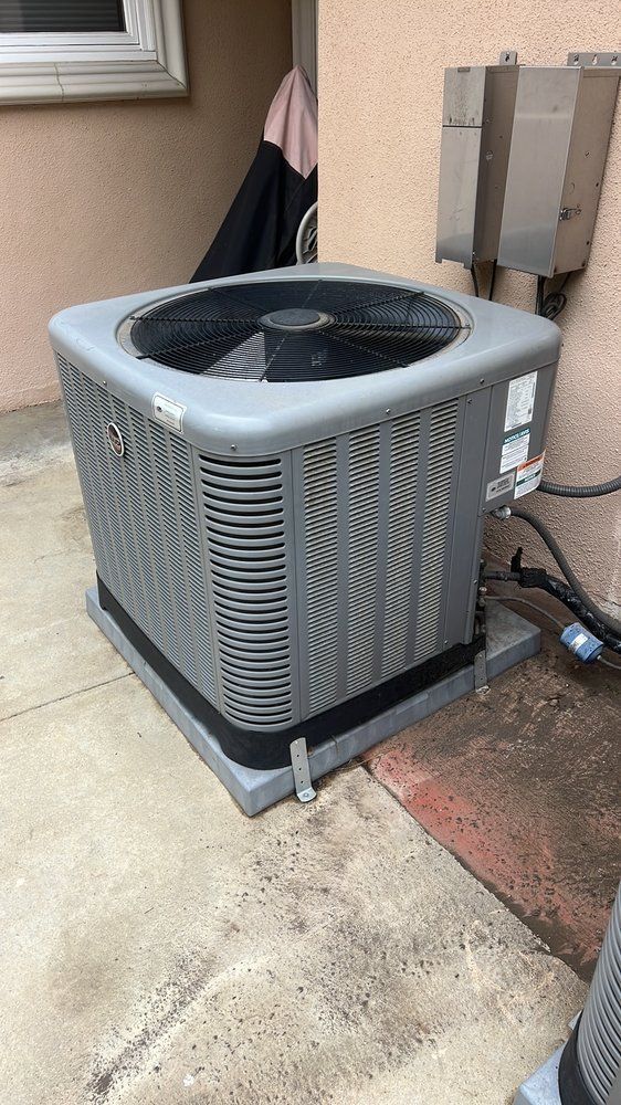 A gray air conditioner is sitting on the side of a building.
