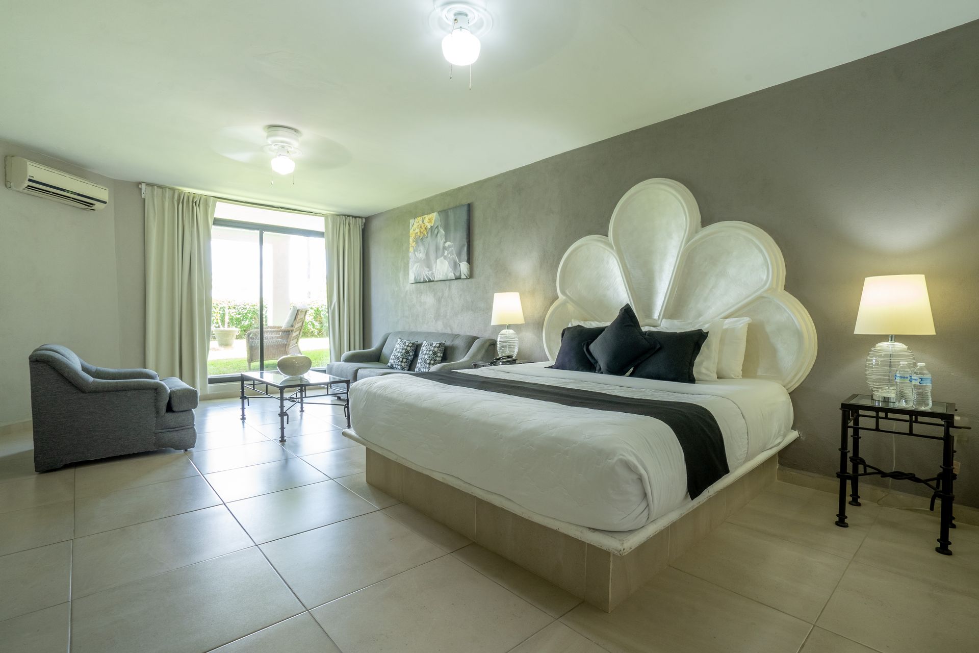 Dormitorio moderno con cama grande, sofá y vista al jardín a través de puertas corredizas.