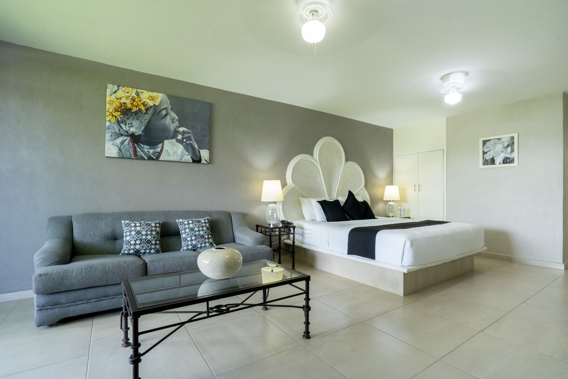 Amplia suite de hotel con una cama, un sofá, una mesa de centro de cristal y arte en una pared gris.